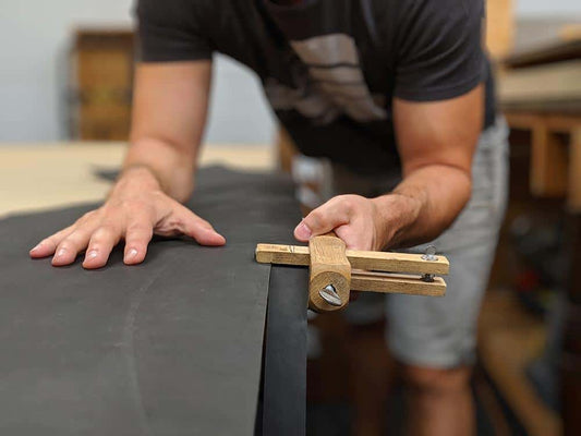 An artist and artisan at work. Bryan using traditional leather working hand tools to cut a hide of slate grey full grain leather