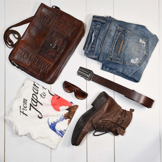 western outfit flat lay including brown leather belt with gun belt buckle, light blue denim jeans, leather cowboy boots, t-shirt and leather handbag