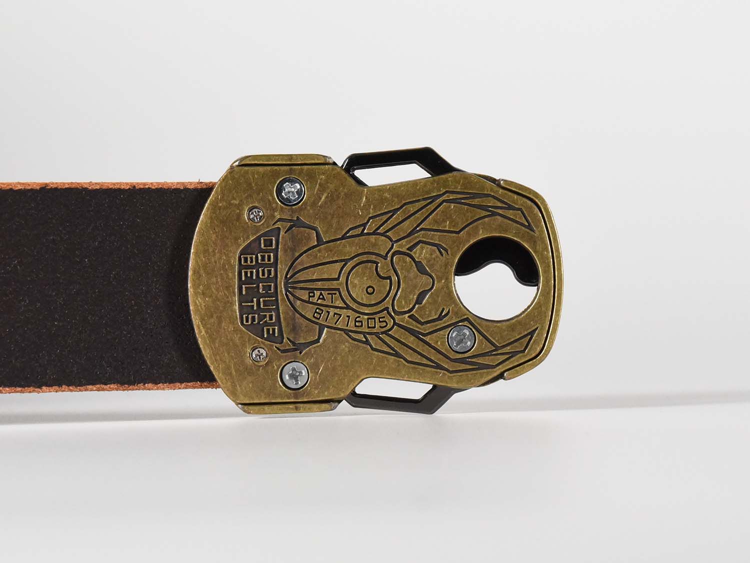 The back of the unique brass belt buckle has an intricate scarab beetle design etched in black with the words "Obscure Belts" and the patent number.