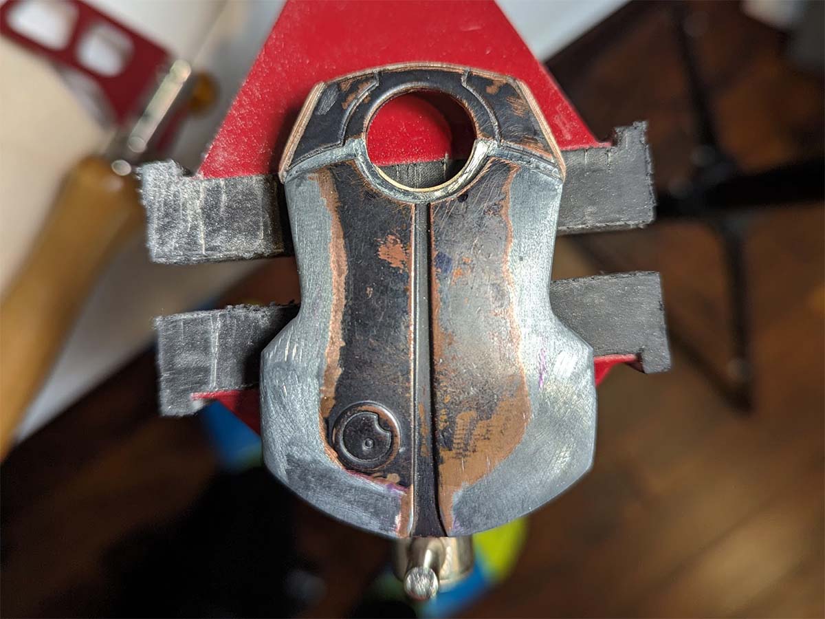 handmade metal prototype of scarab beetle shaped belt buckle with handtools in the background