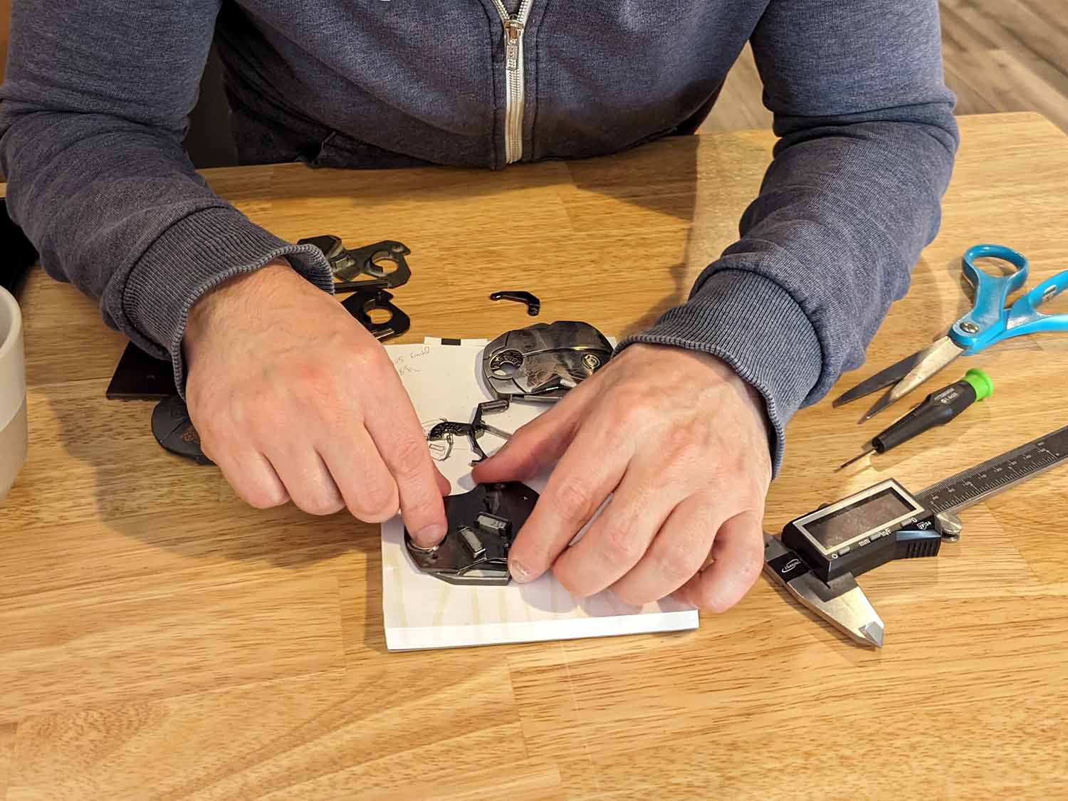 Person working on a small mechanical belt buckle with tools on a wooden table
