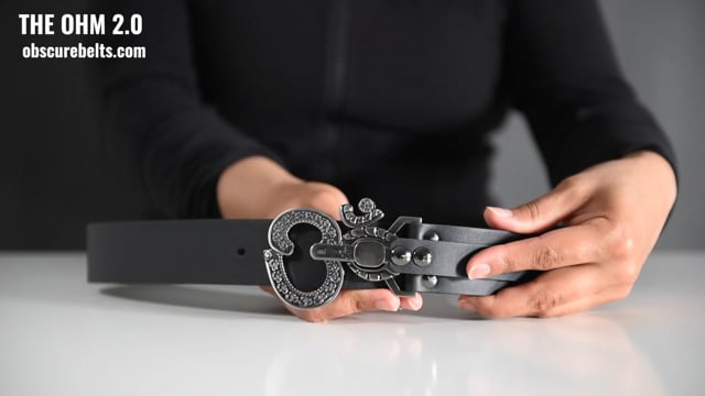 hands showing how to pull the pin to open the ohm 2.0 belt buckle. unscrew the sizing piece to adjust the belt's size