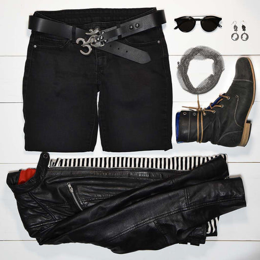 Women's fashion flat lay with black jeans, leather jacket, stripped shirt, leather boots, edgy silver jewelry, sunglasses, and a stylish black leather belt with silver buckle.