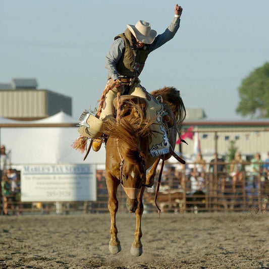 cowboy in a hat riding a bucking bronco at a rodeo