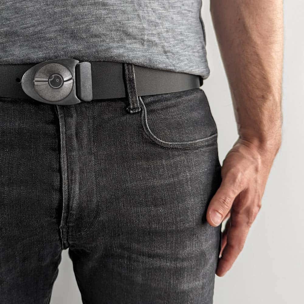 Person wearing unique pewter colored arrowhead shaped belt buckle on a black leather belt with a heathered grey shirt and faded black jeans. The outfit has a monochromatic minimalist vibe.