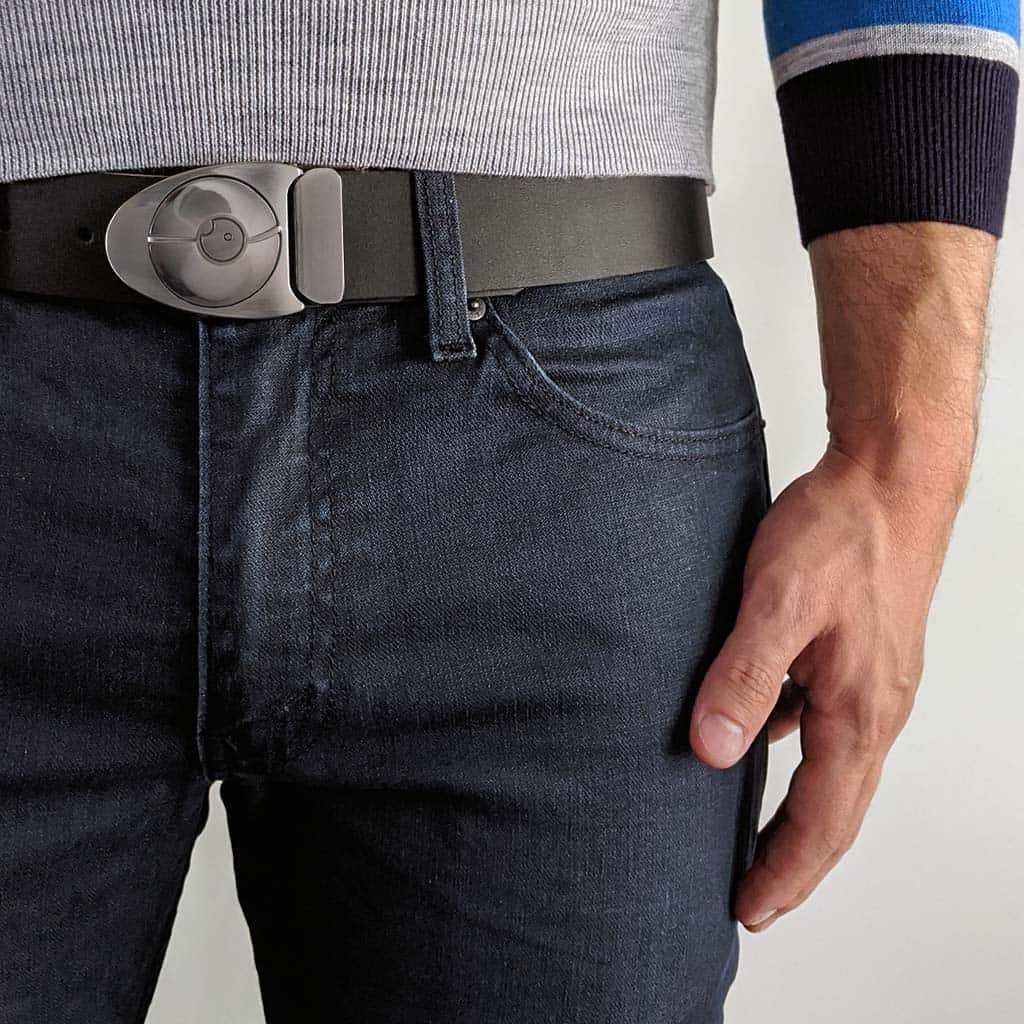 Person wearing small silver belt buckle with black leather belt on dark blue jeans with business casual sweater