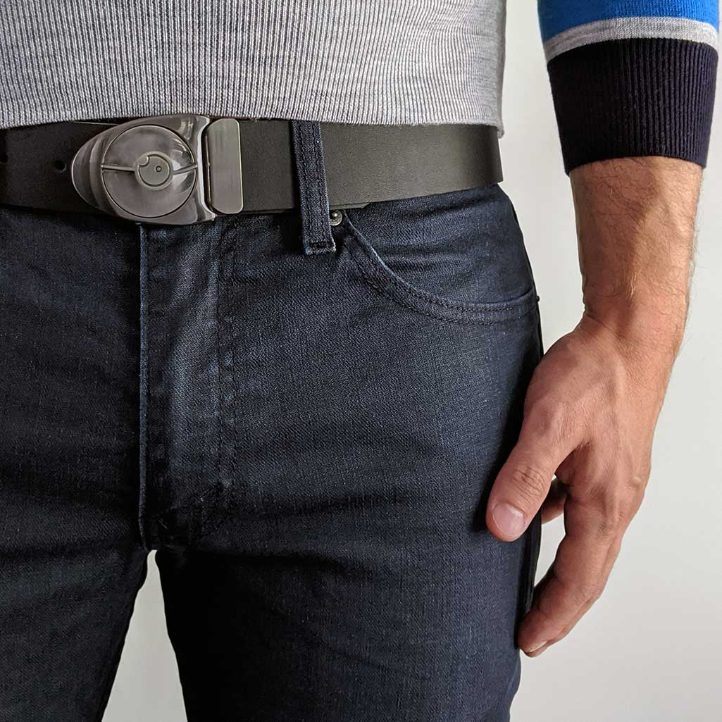 Person wearing silver belt buckle with black leather belt on dark blue jeans with business casual sweater