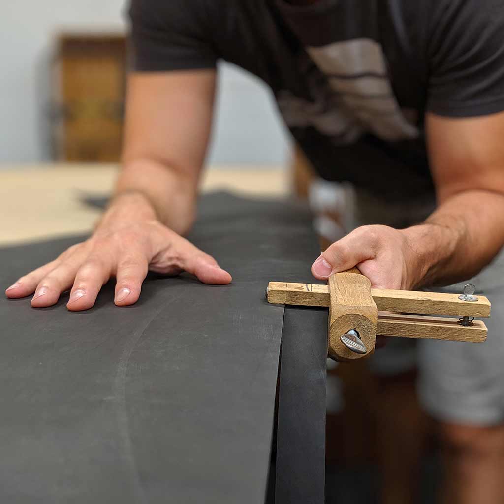 Person using leatherworking tool to handmake a leather belt strap. Our exceptional craftsmanship produces great quality leather goods.