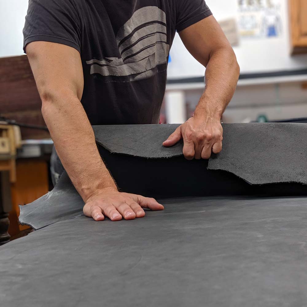 Obscure Belts' Bryan unrolling and inspecting a slate gray full grain leather cow hide