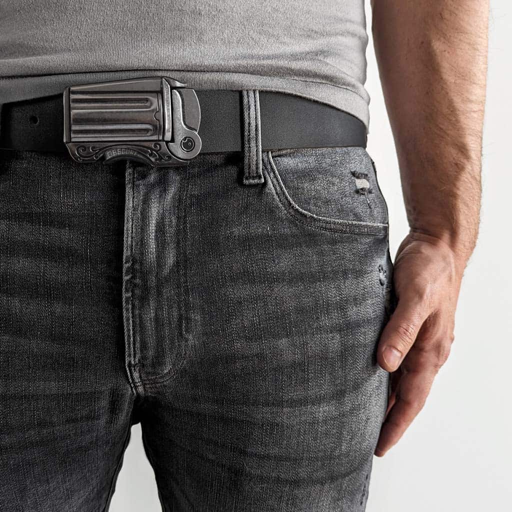 Close up of the waist of a person wearing revolver gun cowboy belt buckles on smooth black leather belt with faded black jeans and a grey t-shirt.
