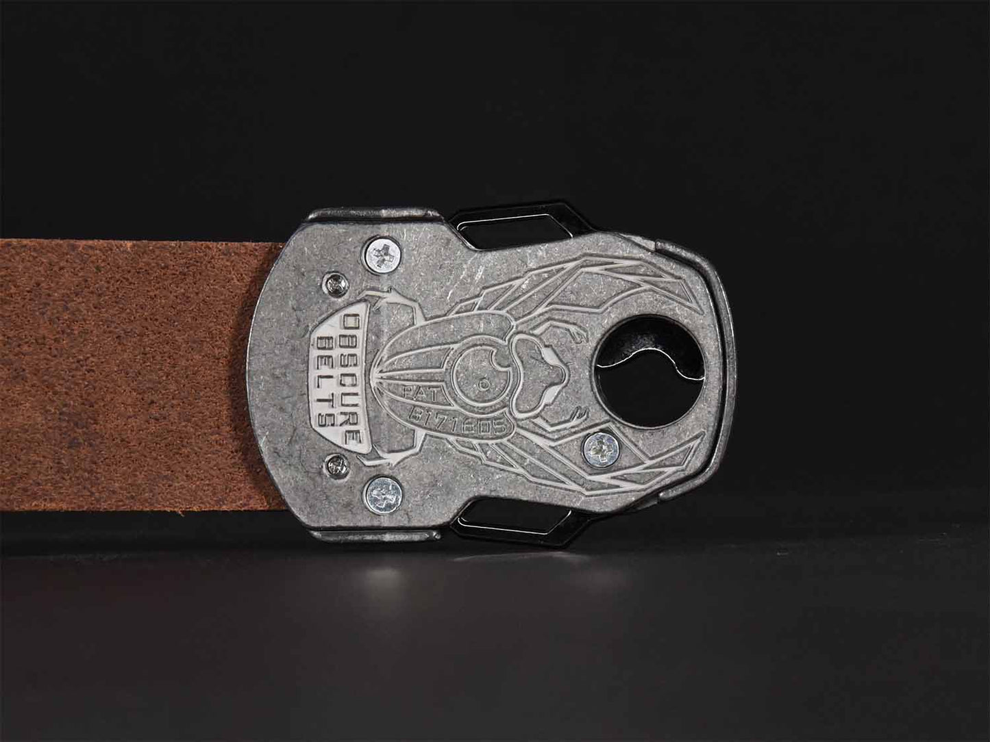 Close up of the back of the unique silver belt buckle with a recessed scarab beetle design etched in white with the words "Obscure Belts" and the patent number.