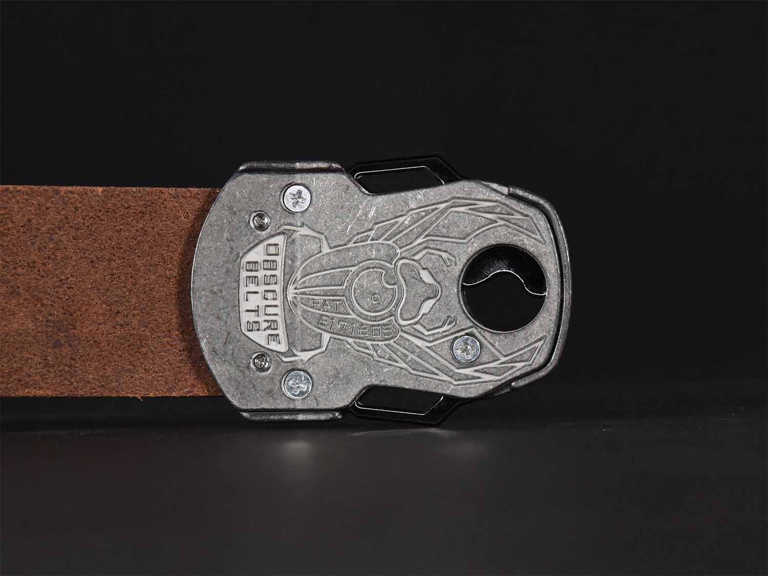 Close up of the back of the unique silver belt buckle with a recessed scarab beetle design etched in white with the words "Obscure Belts" and the patent number.