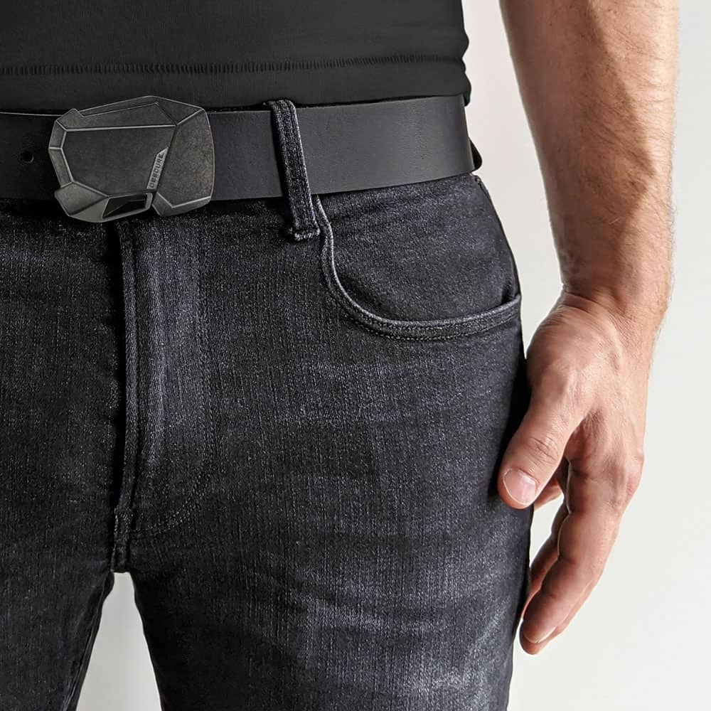 Close up of the waist of a person wearing a futuristic belt buckle on smooth black leather belt with faded grey jeans and a black t-shirt.